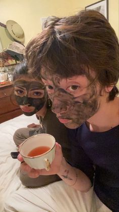 two women with facial masks on their faces holding a cup of tea in front of them