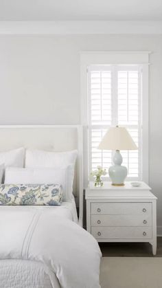 a bedroom with white bedding and two nightstands in front of a large window