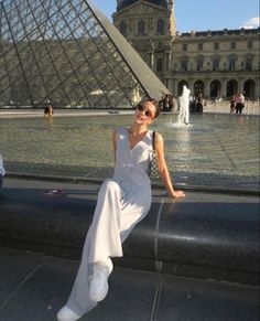 a woman sitting on the edge of a fountain in front of a large glass pyramid