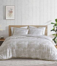 a bed with white sheets and pillows in a room next to a potted plant