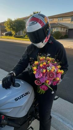 a person wearing a helmet and holding a bouquet of flowers next to a parked motorcycle