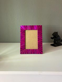 a pink and purple photo frame sitting on top of a table next to a black bear