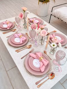 the table is set with pink and white plates, silverware, and napkins