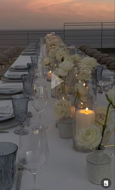 a long table is set with white flowers and candles for an elegant dinner on the deck