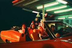 a group of people sitting in the back of a red convertible car at night time