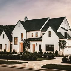 a large white house with lots of windows and bushes in front of it at dusk