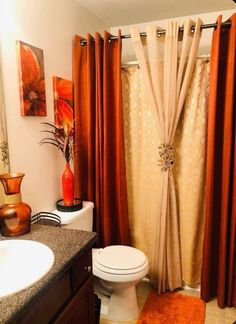 a bathroom with a toilet, sink and shower curtained in oranges and browns