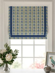 a window with a blue and green roman blind on it's side, next to a vase with flowers