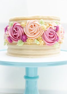 a white cake with pink frosting and flowers on it sitting on a blue plate