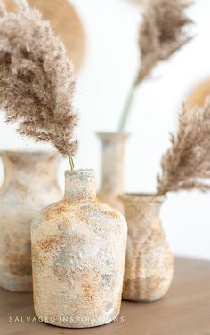 three vases with dried plants in them on a table