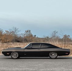 a black car is parked on the side of the road in front of some dry grass