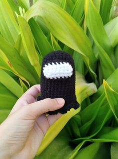 a hand holding a small crocheted object in front of some green plants and grass