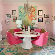 a dining room table with pink chairs and pictures on the wall in front of it