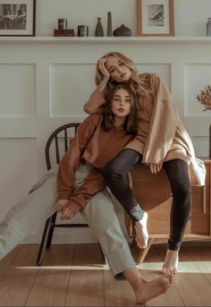 two women are sitting on the back of a chair in front of a wall with pictures