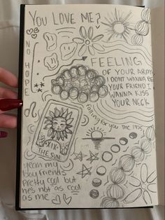 someone's hand holding up a notebook with doodles on the pages and writing