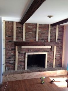 an empty room with a brick fireplace and wood beams on the ceiling, surrounded by construction materials