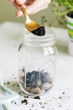 a person holding a spoon over a jar filled with dirt