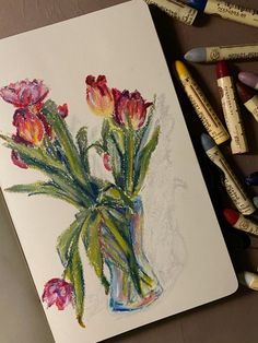 some crayons are next to a drawing of tulips in a vase