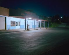 an empty parking lot at night in front of a building with two gas pumps on it