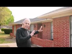 a man standing in front of a red brick house holding his hand up to the camera