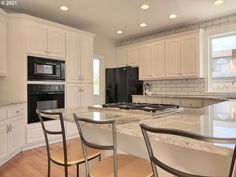 a kitchen with white cabinets and marble counter tops, black appliances and an island in the middle