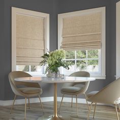 a dining room table with four chairs and a vase on the table in front of two windows