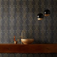 a bathroom with black and gold wallpaper and two lights above the sink in front of it