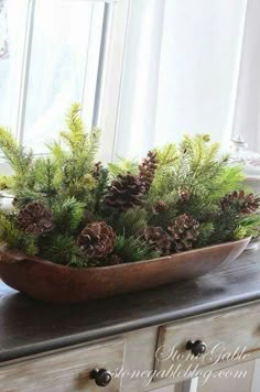 a wooden bowl filled with pine cones and greenery sitting on top of a table