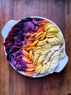 a bowl filled with different colored vegetables on top of a wooden table