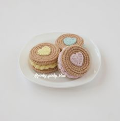 three crocheted cookies on a white plate with hearts in the middle and one cookie shaped like a heart