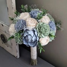 a bridal bouquet with blue flowers and greenery is displayed in front of an open door