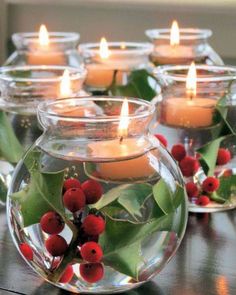 candles are lit in glass bowls with holly and berries