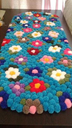 a crocheted blanket with flowers on it sitting on top of a wooden table