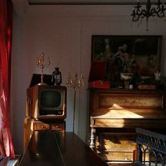 an old fashioned tv sitting on top of a wooden table in front of a piano