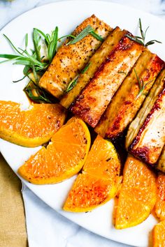 grilled meat and orange slices on a plate with rosemary garnish, ready to be eaten