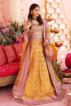 a woman in a yellow and pink lehenga standing next to a red couch