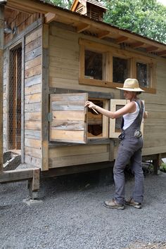 a woman wearing overalls and a straw hat standing in front of a small wooden cabin