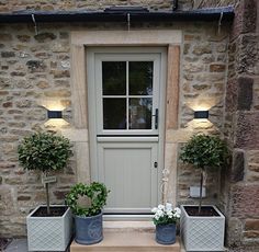 two planters are sitting in front of the door to a stone building with potted plants