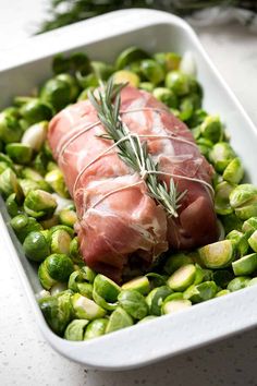 a white dish filled with brussel sprouts and ham