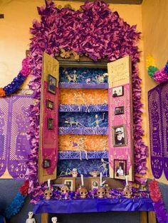 an altar with purple flowers and pictures on it's walls, decorated in bright colors