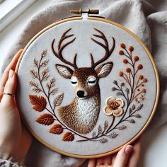 someone is holding up a hand embroidered deer head with flowers and leaves on the hoop