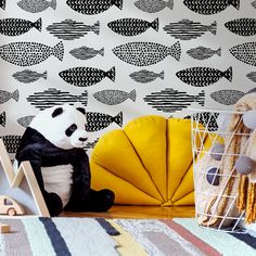 a stuffed panda bear sitting on the floor next to a wallpaper with fish design