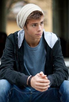 a young man sitting on the ground wearing a beanie and looking to his left