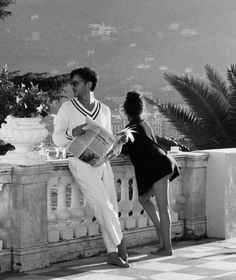 a man standing next to a woman on top of a stone wall with palm trees in the background