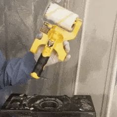 a man in blue shirt and white gloves holding a yellow paint roller over a black box