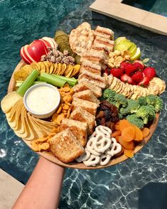 a platter with fruit, vegetables and crackers next to a swimming pool