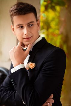 a young man wearing a suit and tie with his hands on his chin looking at the camera