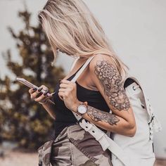 a woman with tattoos on her arm looking at her cell phone while holding a bag