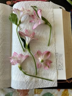 some pink flowers are on top of a white towel next to an open book that is sitting on a floral print tablecloth