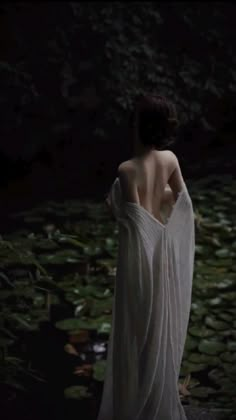 a woman in a white dress is standing near lily pads and water lillies at night